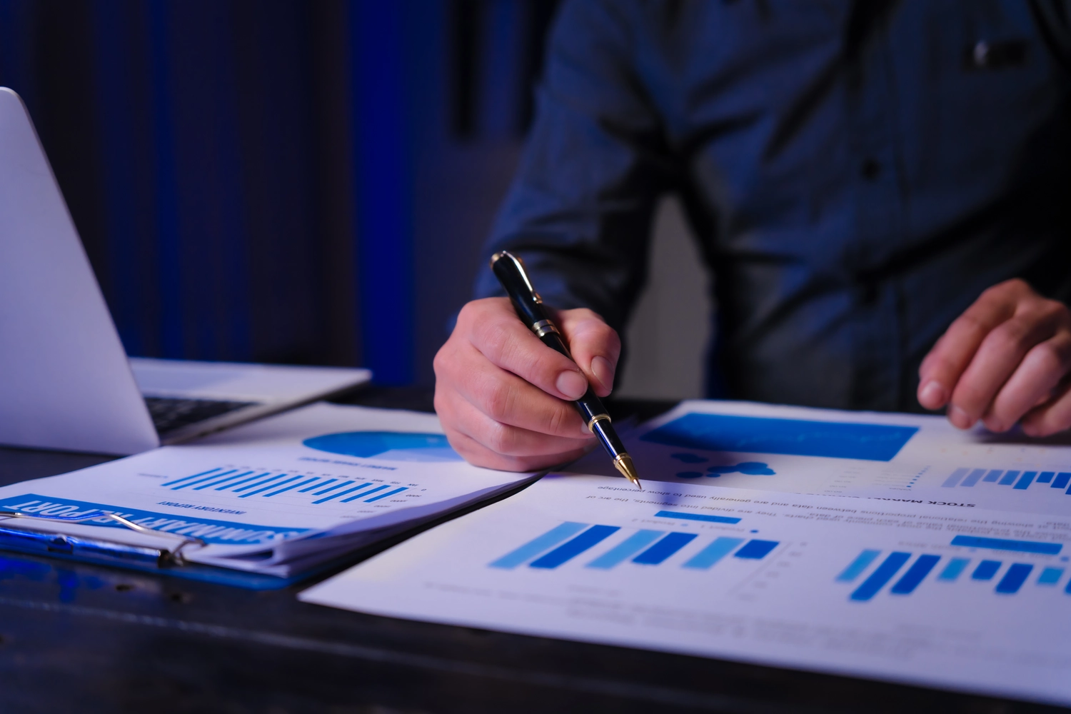 Ein Mann arbeitet spät abends an seinem Schreibtisch und blickt in Diagramme und Dokumente. Er führt Datenanalysen und strategische Planungen im Rahmen der Politik- und Planungsabteilung durch.